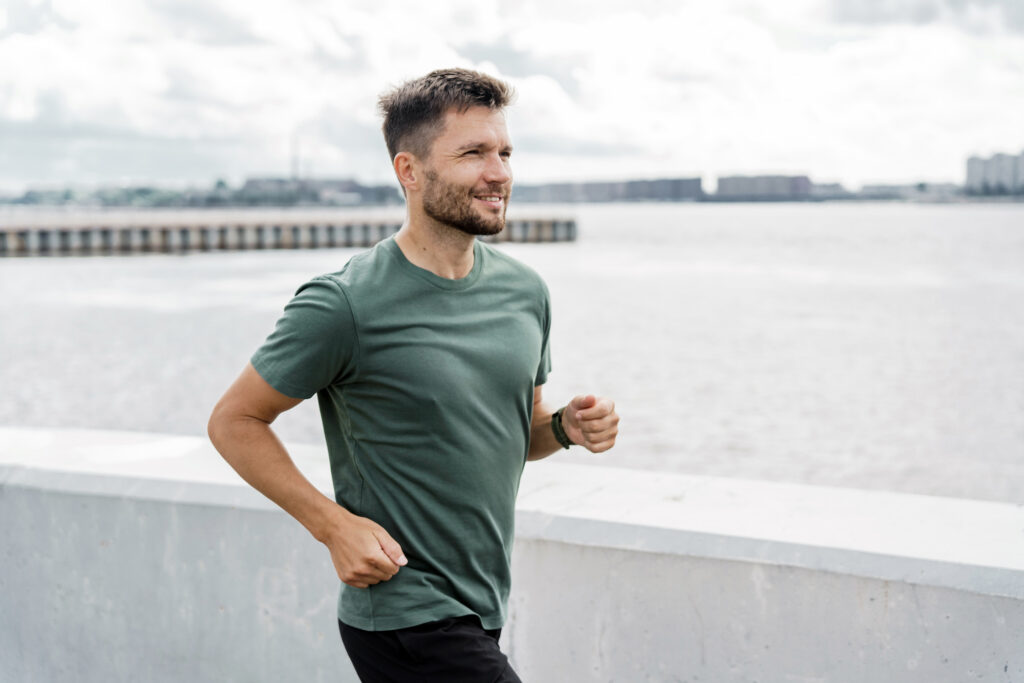 man in a green t-shirt jogs in front of the water